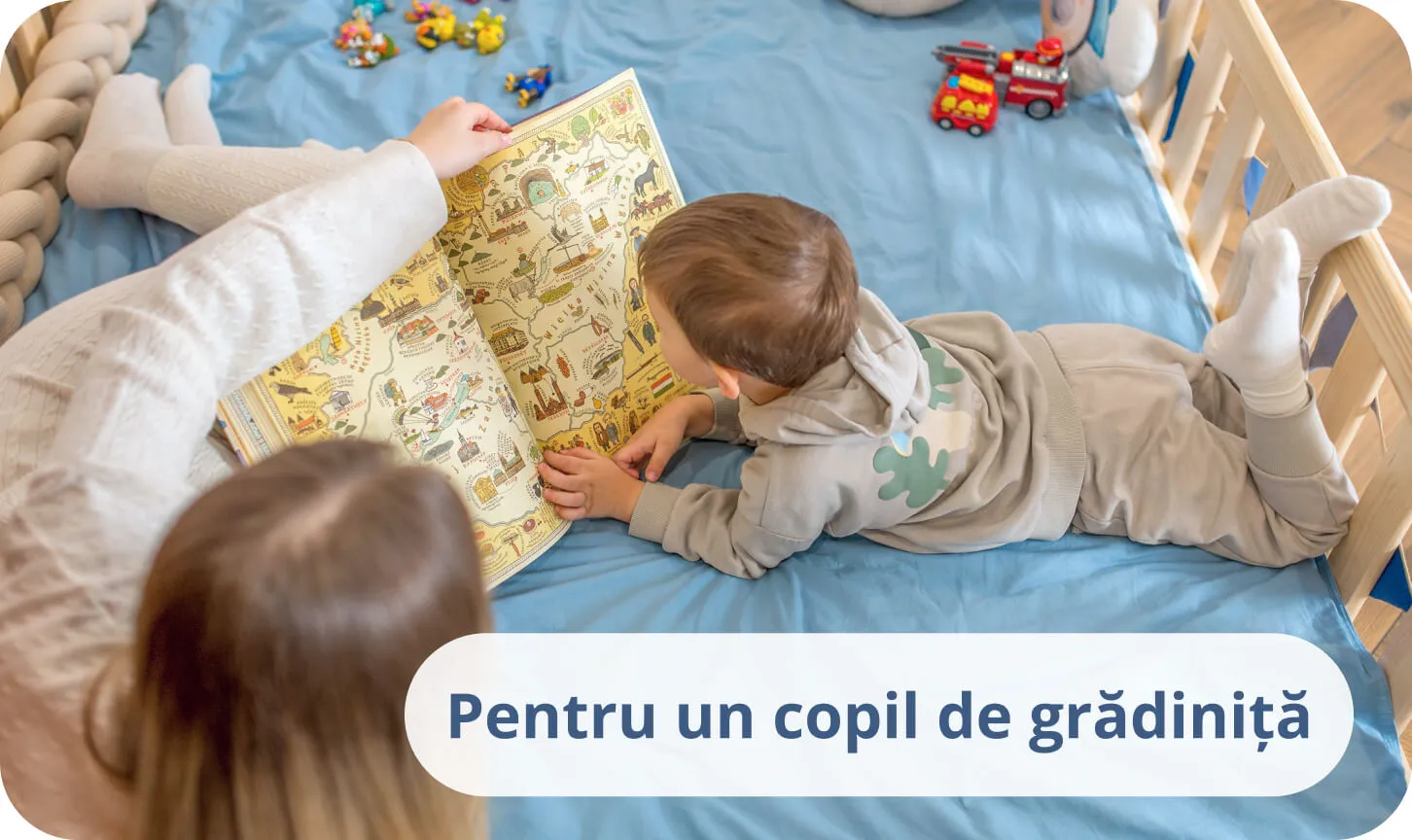Băiețel cu mama sa citind o carte colorată pe lenjerie albastră într-un pat din lemn de pin.